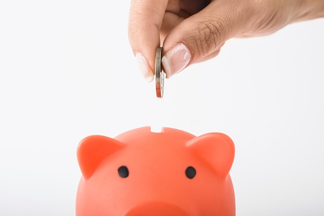 A hand placing a coin into a piggy bank, symbolizing traditional savings habits and long-term wealth building.